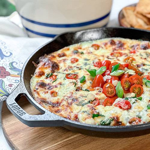 Side view of Hot Caprese Dip in a cast iron skillet garnished with cherry tomatoes and green onions.