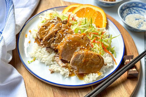 Horizontal view of sliced Crockpot Pork Tenderloin with Orange Ginger sauce over rice with fresh orange slices.