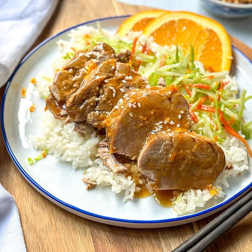 Horizontal view of sliced Crockpot Pork Tenderloin with Orange Ginger sauce over rice with fresh orange slices.