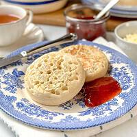Side view of two crumpets on a blue and white plate with strawberry jam.