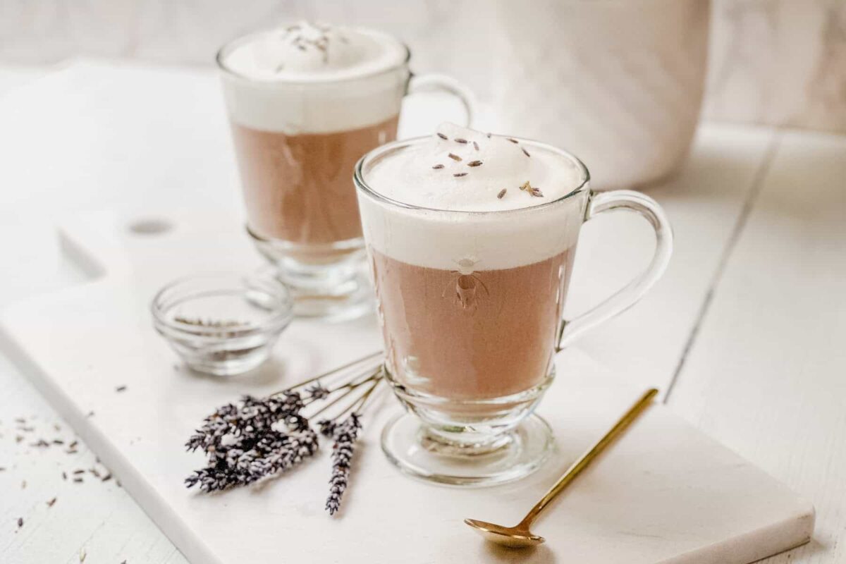 Horizontal view of two glass mugs of Lavender Earl Grey Tea Latte with foamed cream and dried culinary lavender.