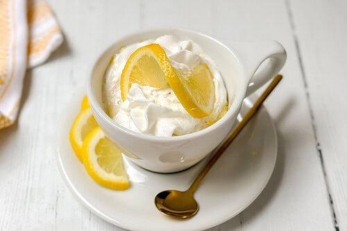 Side horizontal view of lemon mug cake in a white mug with a twist of lemon and a small gold spoon.