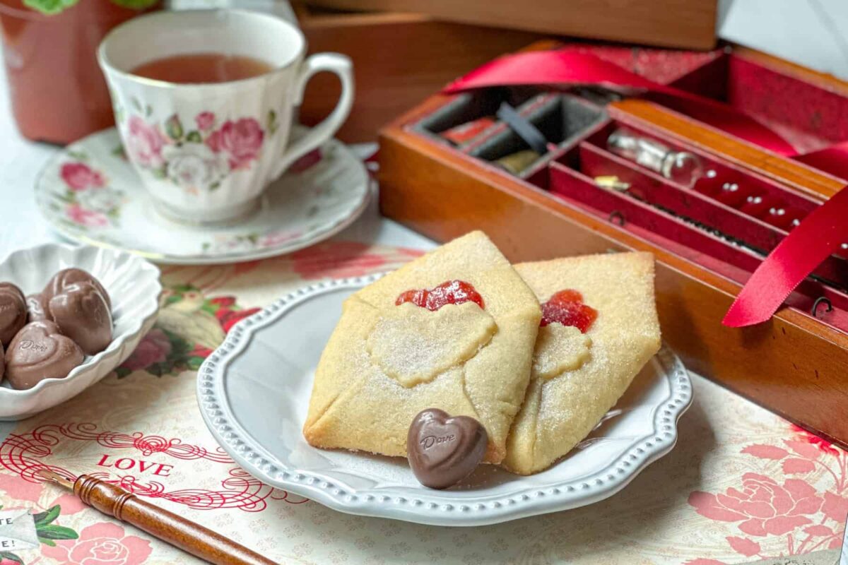 Close up side view of Love Letter Butter Cookies on a white plate with a milk chocolate heart-shaped candy.
