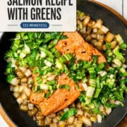 Pan seared salmon fillets with chopped greens and diced onions sizzle in a skillet, accompanied by small bowls of pepper and crushed red pepper on the side.
