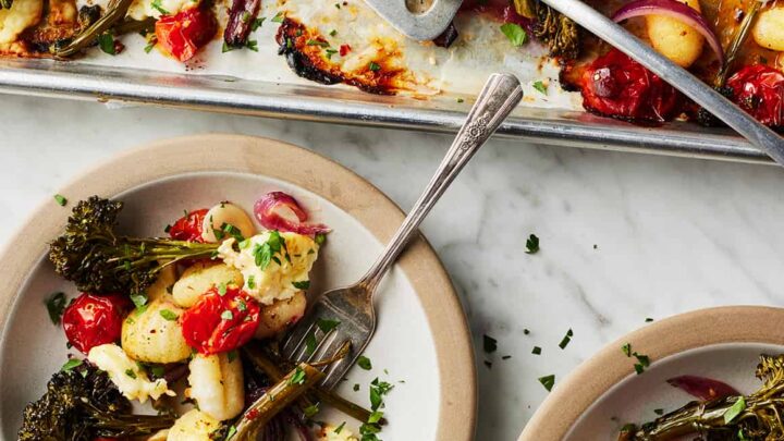 Top view of two servings of sheet pan gnocchi with silver forks and more on a silver sheet pan.