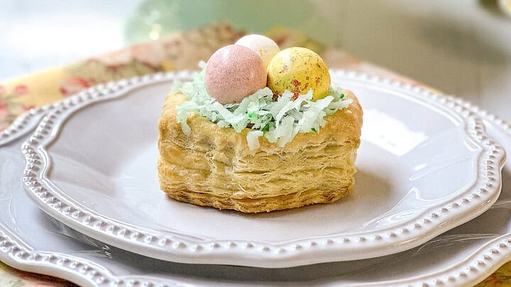 Side view of Easter Basket puff pastry tarts on a white plate with more in the background on a mini teal cake stand for teatime.
