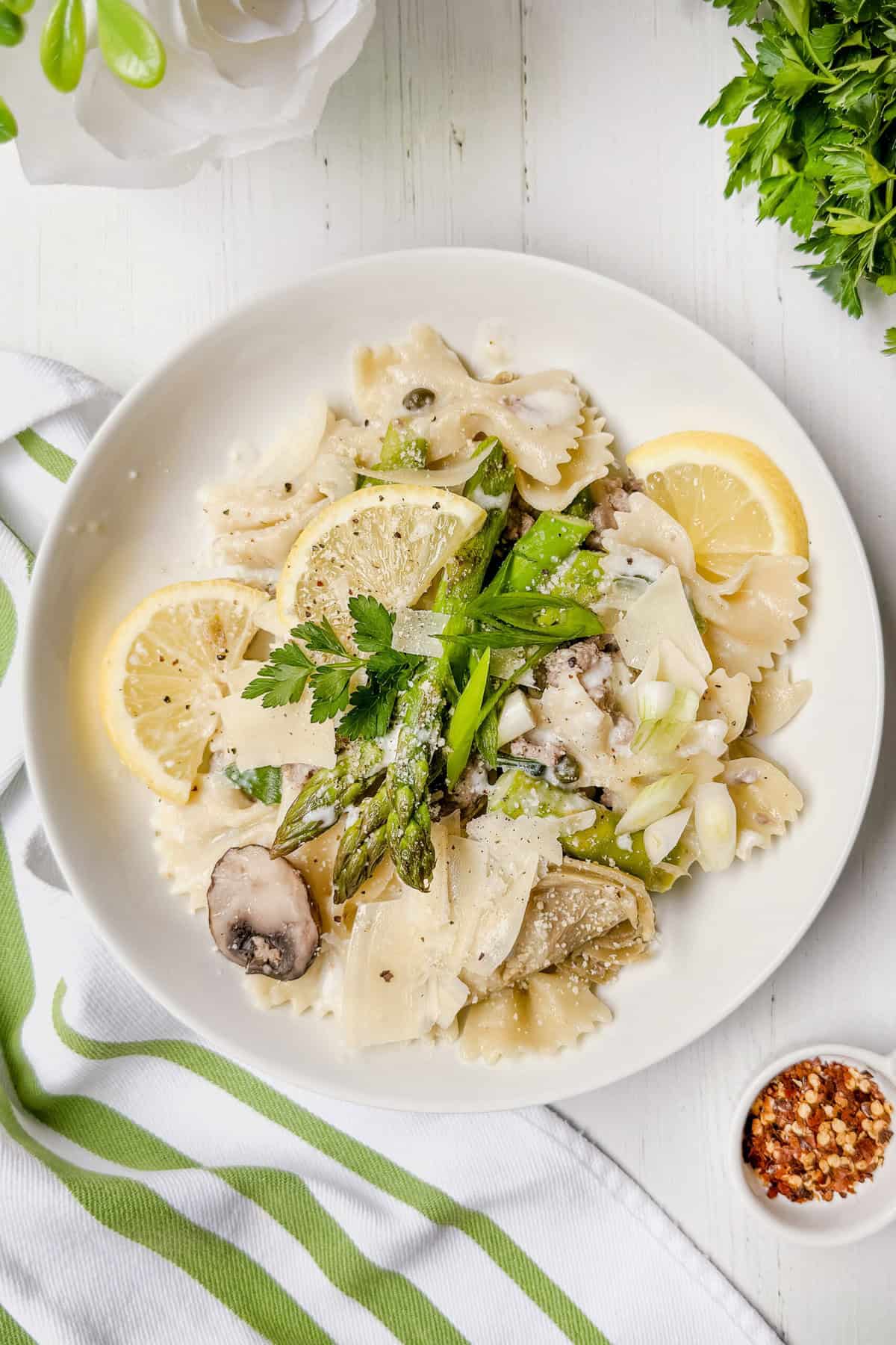 Top view of One Pot Asparagus Pasta on a white plate with lemon slices and parsley.