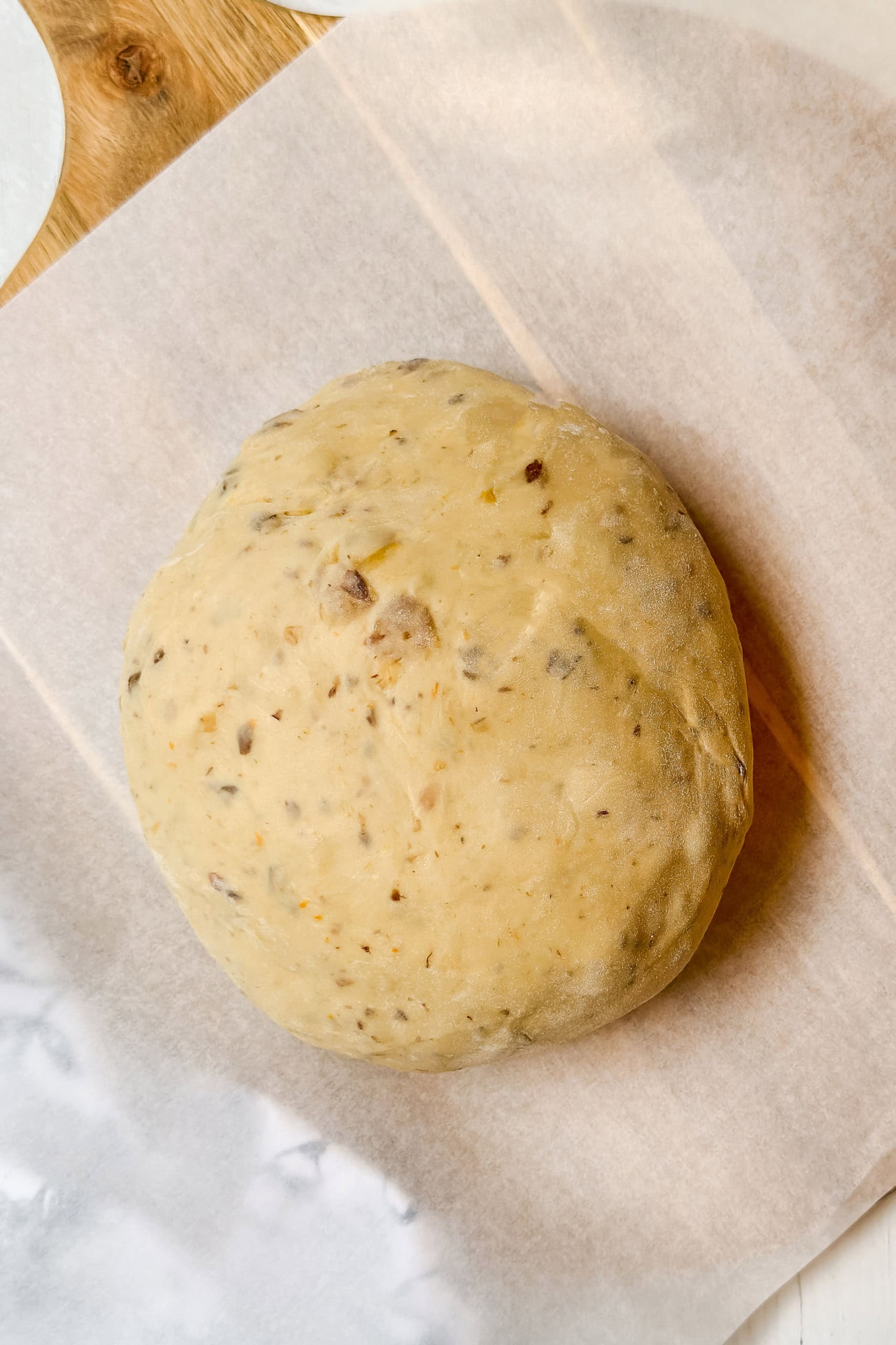 A round ball of dough, reminiscent of German Easter Bread, with visible seeds or grains sits on a sheet of parchment paper.