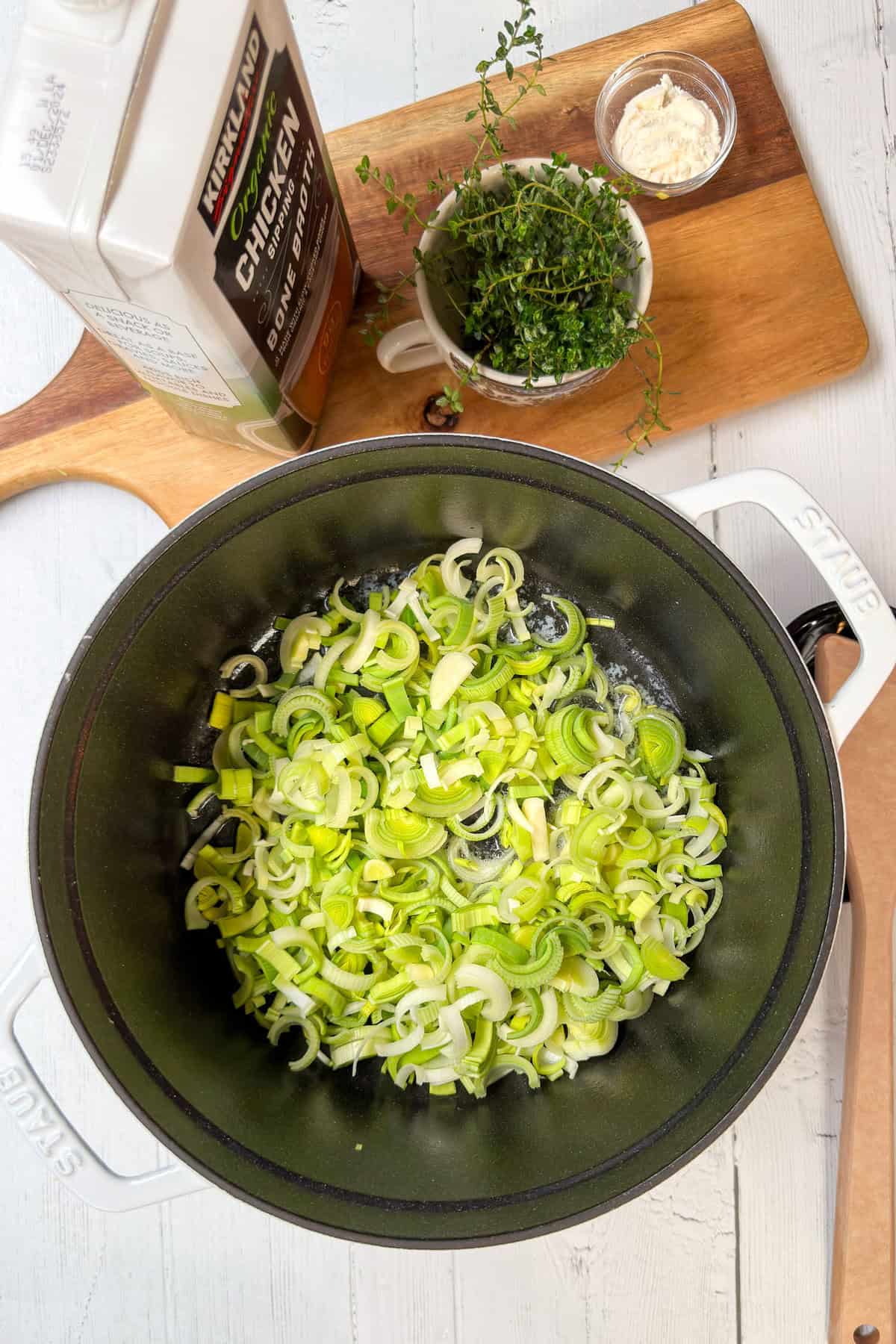 Top view of chopped leeks in a large Dutch oven pan with fresh thyme.