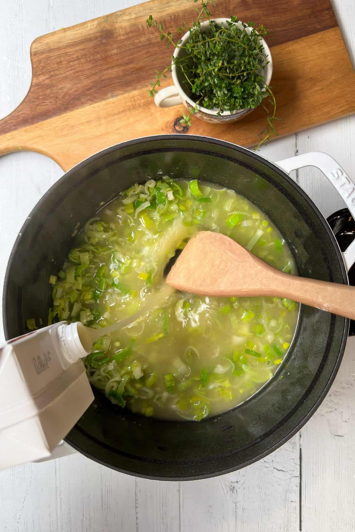 Top view of broth being poured into Potato Leek Soup cooking in a white Dutch oven.