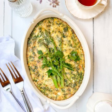 Asparagus egg bake casserole in baking dish topped with fresh herbs and cheese.