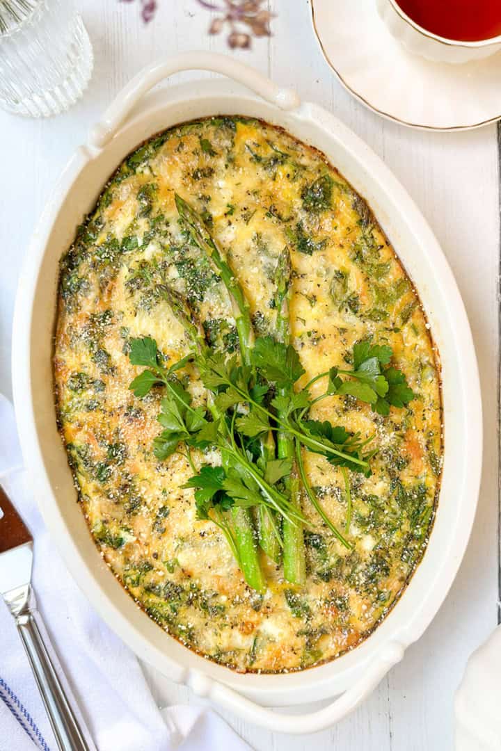 Asparagus egg bake casserole in baking dish topped with fresh herbs and cheese.