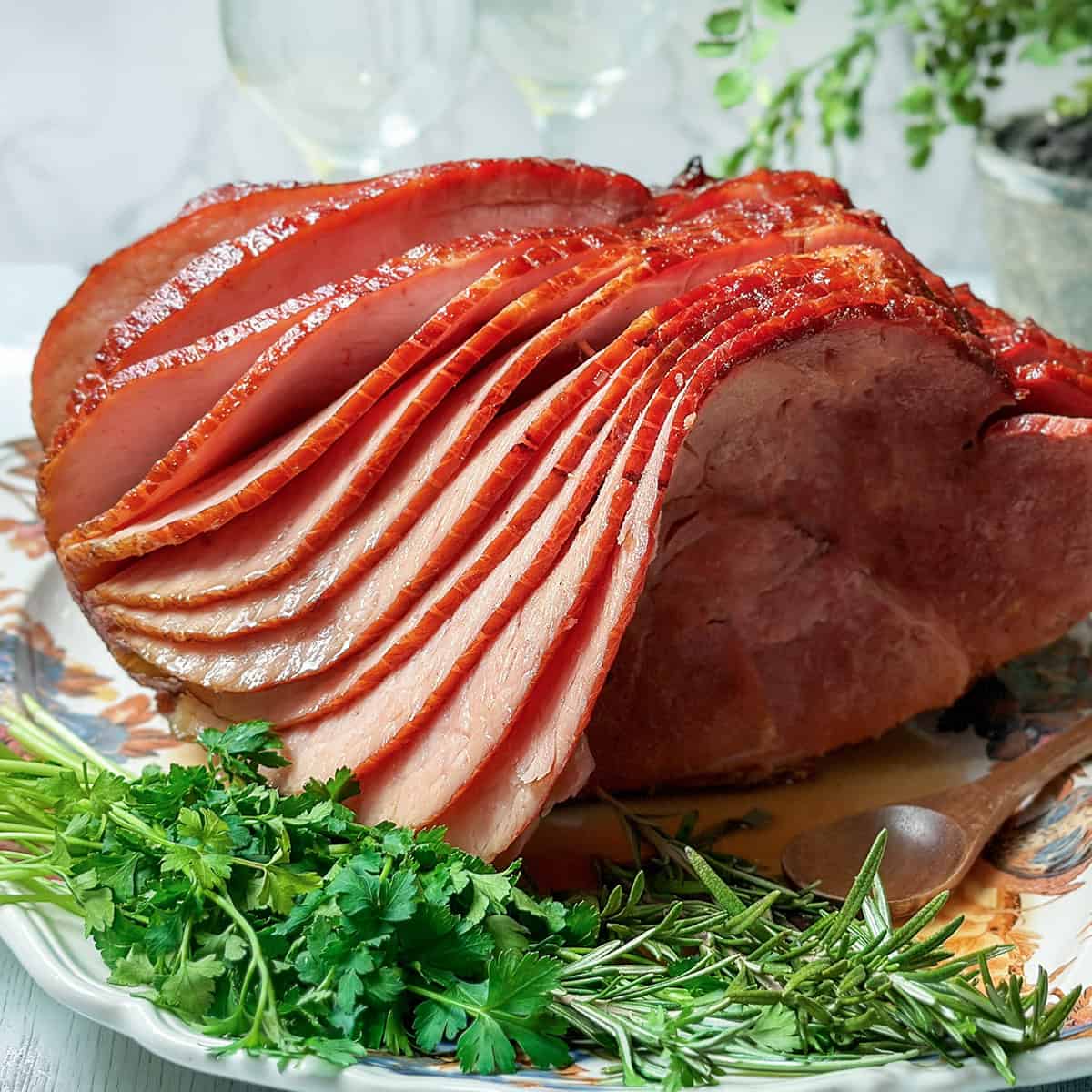 Sliced honey baked ham served on a platter with fresh parsley and rosemary garnishes.