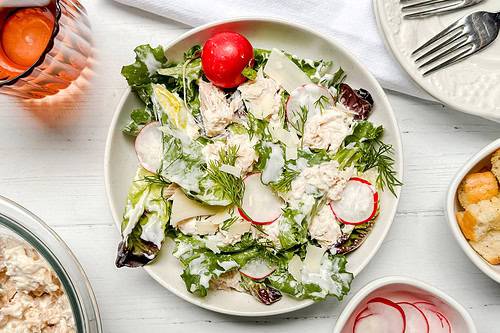 Top view of Tuna Salad on a white plate with greens, fresh herbs, and sliced radishes.