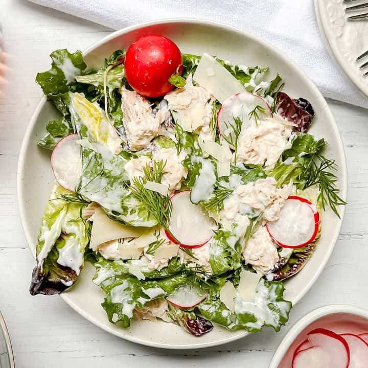 Top view of Tuna Salad on a white plate with greens, fresh herbs, and sliced radishes.