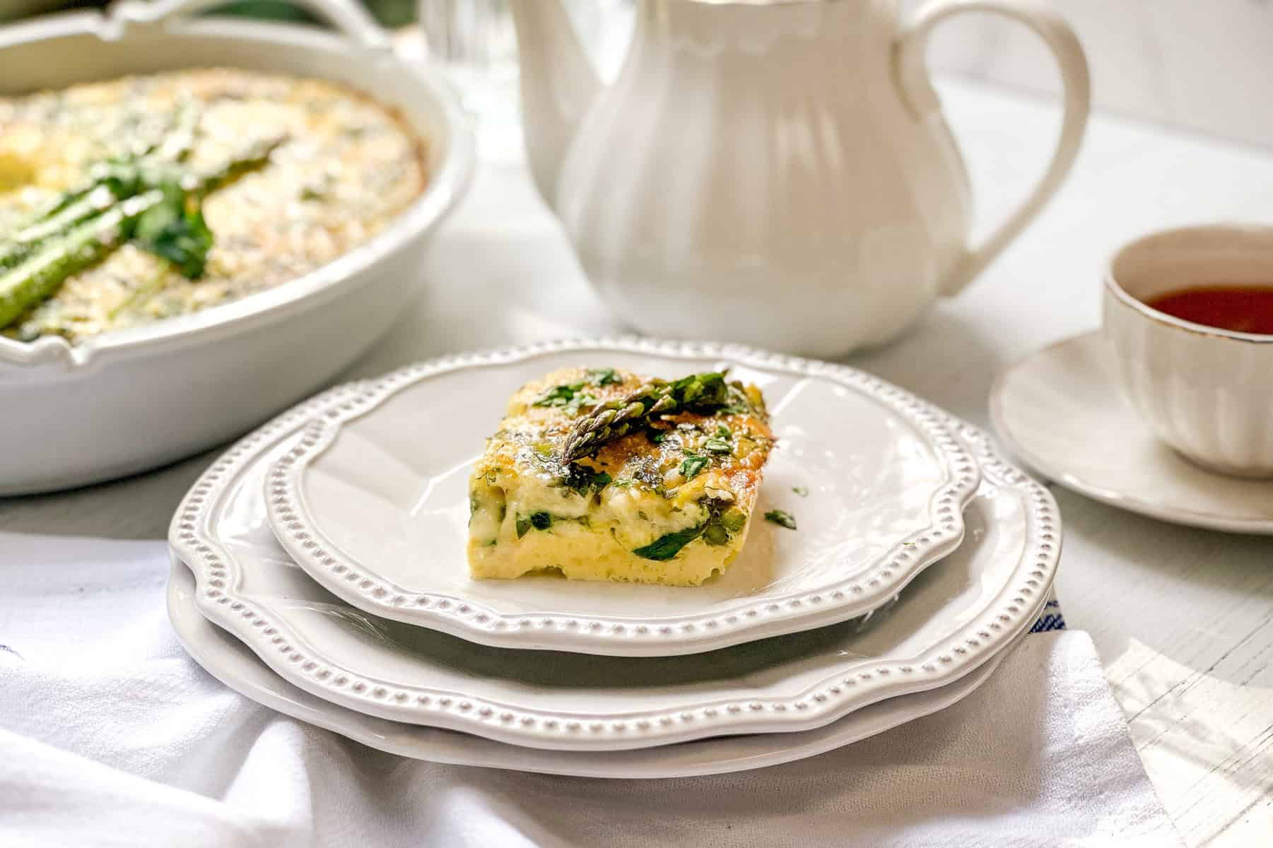 Horizontal view of a brunch serving of Asparagus Egg Bake Casserole with a white teapot in the background.