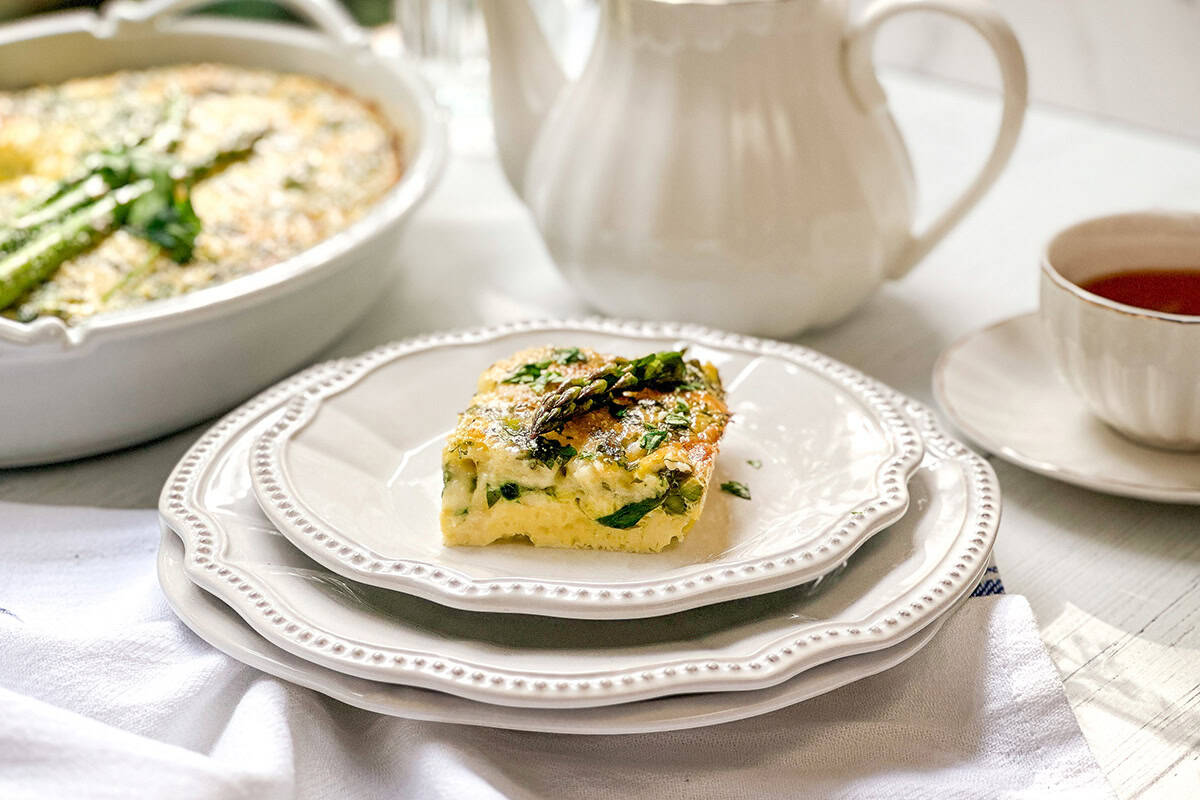 Asparagus egg bake casserole slice served on plate with baking dish and tea in background.