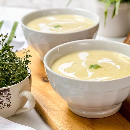 Horizontal view of two white bowls filled with Potato Leek Soup with fresh thyme leaves.