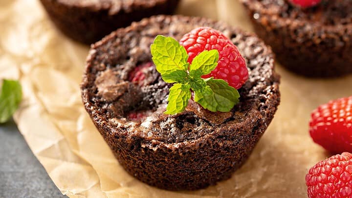 Horizontal side view of brownie bites with mint and fresh raspberries.