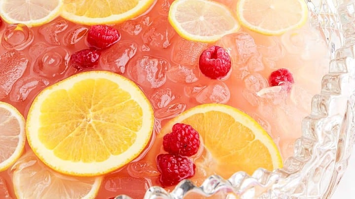Closeup view of red party punch with red raspberries and lemon slices in a glass serving bowl.