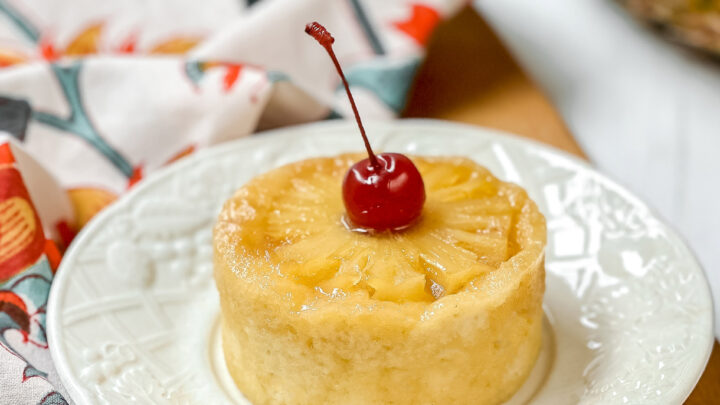 Side top view of Pineapple Upside Down Mug Cake on a white plate sitting on a wooden cutting board.