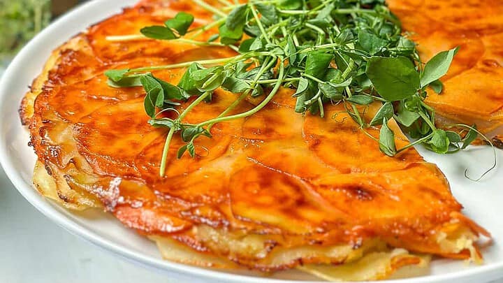 Side view of Sweet Potatoes Anna on a white serving stand with fresh green pea shoots for garnish.