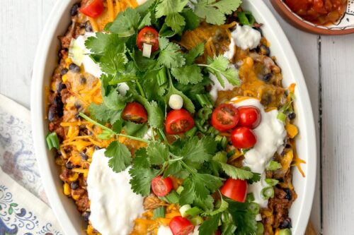 Top view of taco casserole with fresh cilantro, cherry tomatoes, green onions, and Greek yogurt as garnish.
