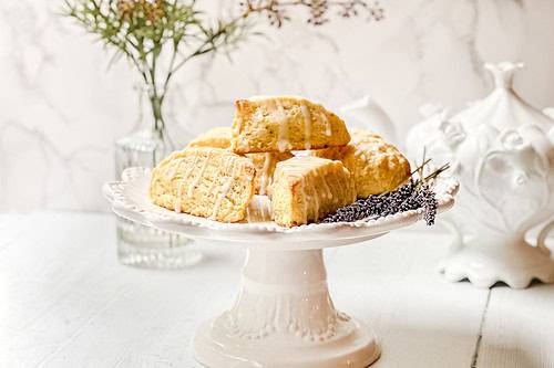 Side view of Lemon Lavender Scones with fresh lavender on a white cake stand in front of a marble background.