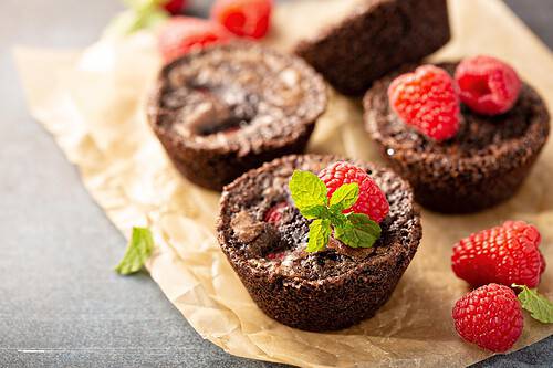 Horizontal view of homemade brownie bites on parchment and garnished with fresh raspberries and mint leaves.