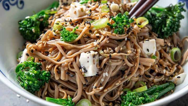Distance view of whole grain sesame noodles with chop sticks, green broccoli and white goat cheese.