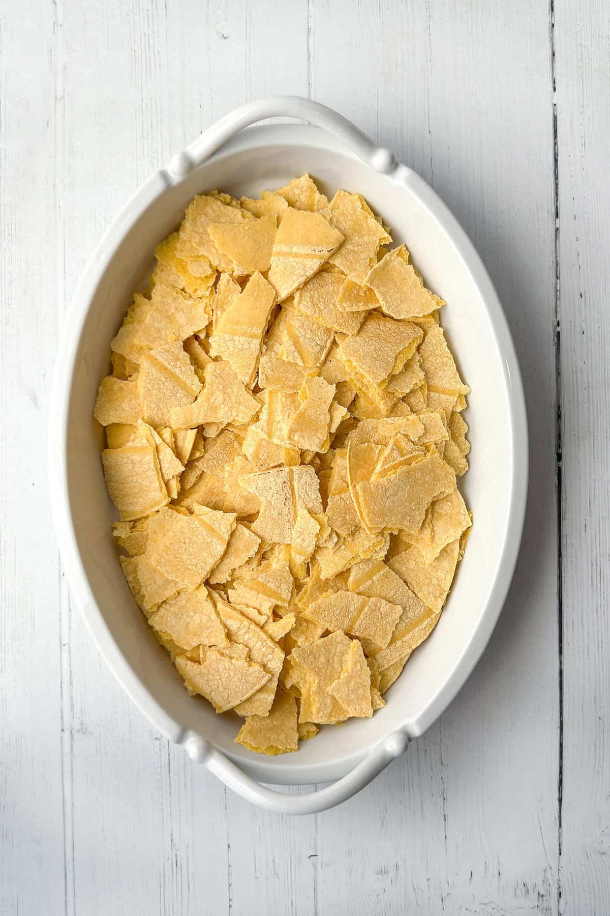 Layering corn tortillas in an oval baking dish.