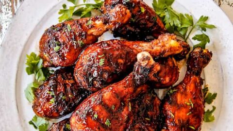 Closeup top view of BBQ chicken drumsticks on a white plate with fresh parsley.