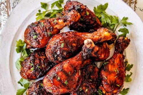 Closeup top view of BBQ chicken drumsticks on a white plate with fresh parsley.