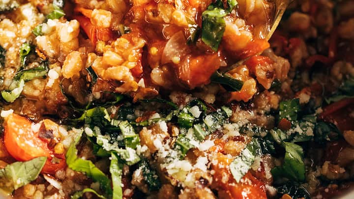A close-up of a pot of tomato risotto with fresh basil and grated cheese, with a spoon lifting a portion—perfect for easy One Pot Dinners in May.