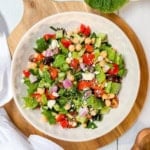 A plate of Mediterranean Chopped Salad with lettuce, cherry tomatoes, cucumber, red onion, chickpeas, black olives, and feta cheese on a wooden board.