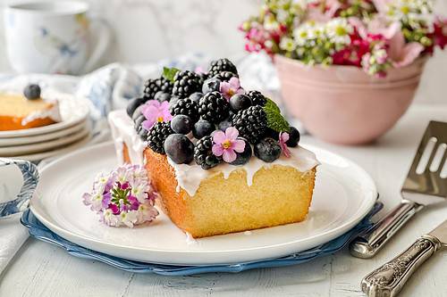 Horizontal side view of sliced pound cake with icing and topped with fresh berries on a white serving plate.