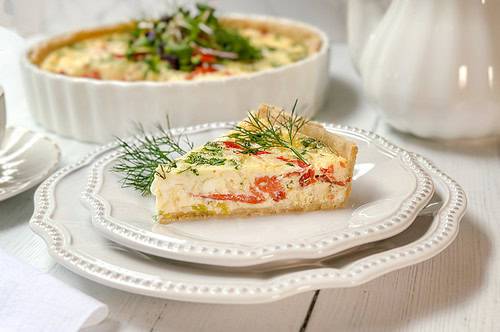 Horizontal view of sliced salmon quiche on a white plate with fresh dill on top.