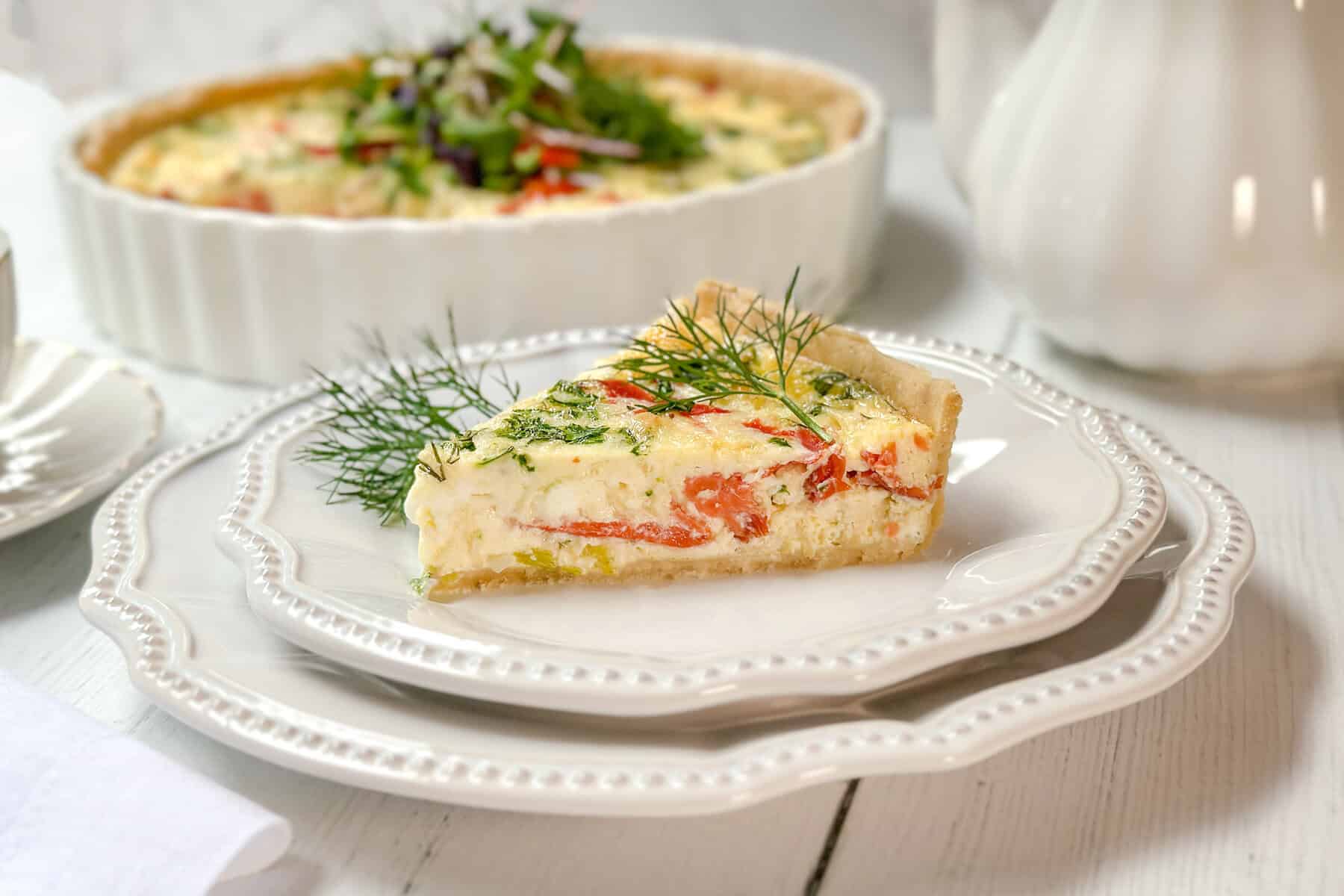 Horizontal view of sliced salmon quiche on a white plate with fresh dill on top.
