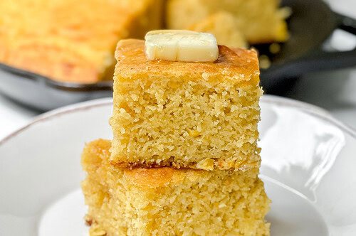 Side view of two stacked squares of cornbread on a white plate.