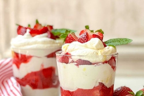 Side view of two Eton Mess glasses on a white background with a red and white striped towel and a grey background.