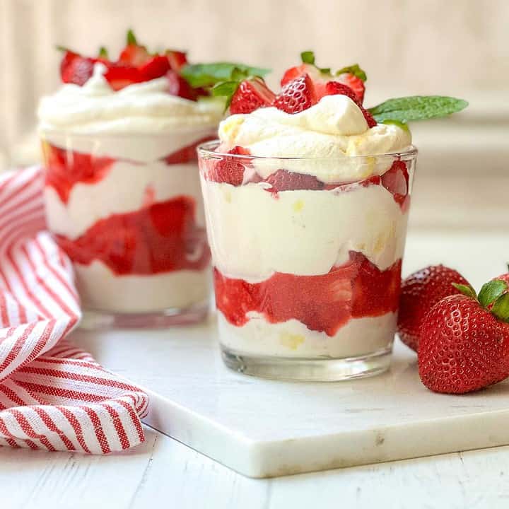 Side view of two Eton Mess glasses on a white background with a red and white striped towel and a grey background.