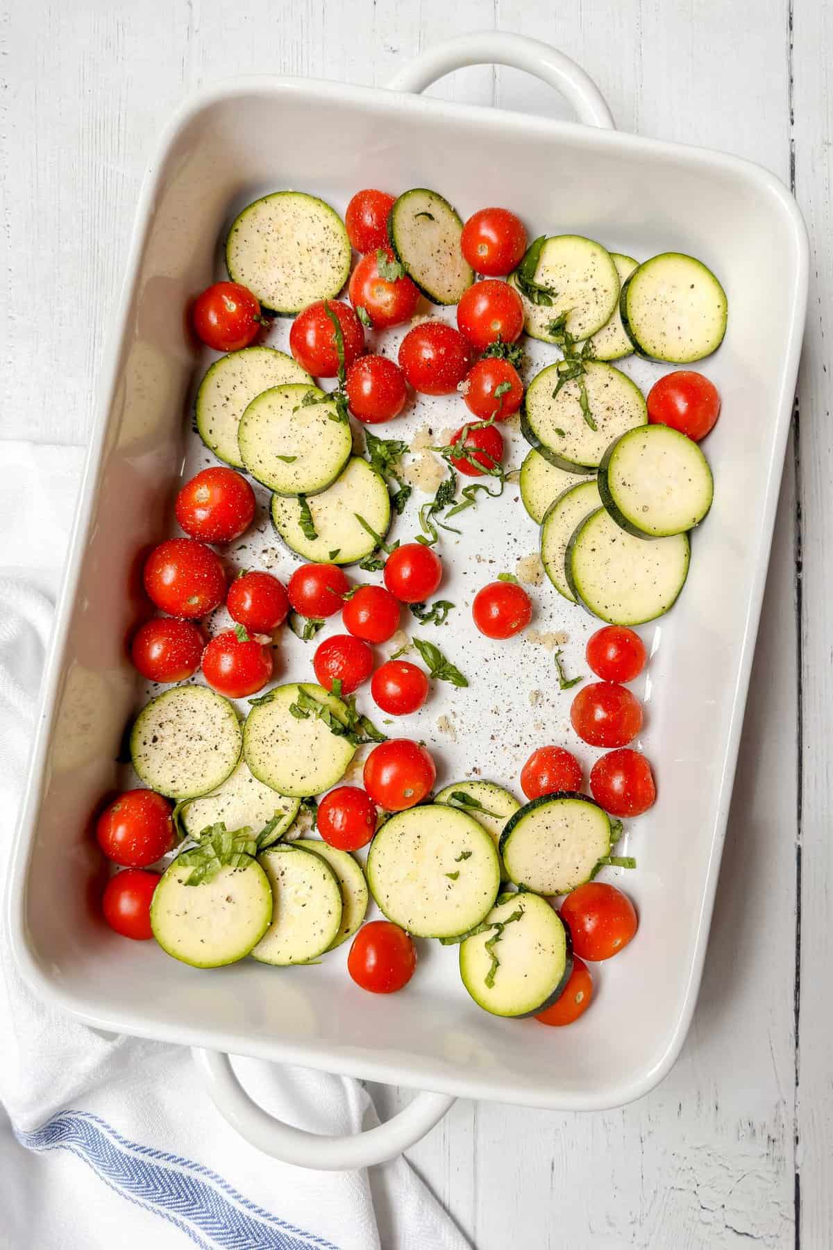 Top view of veggies and seasoning in a white casserole dish.
