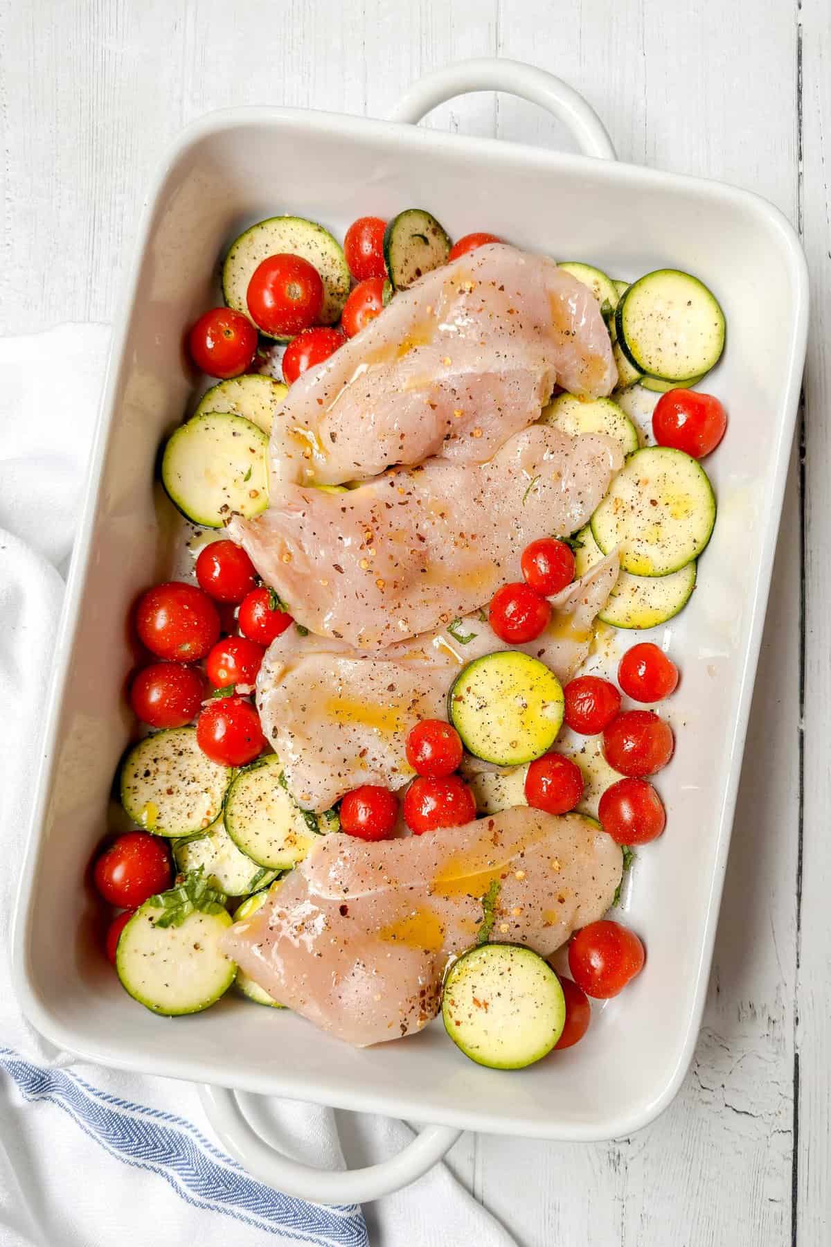 Top view of unbaked chicken breasts in white casserole dish.