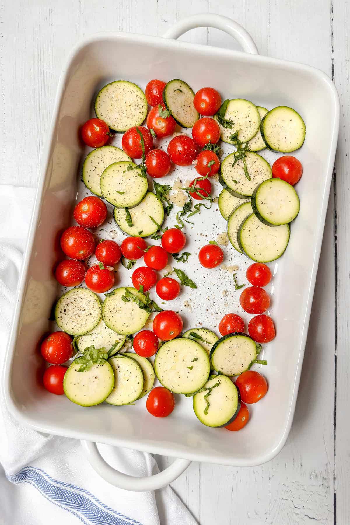 Pesto Caprese Chicken uncooked vegetables in baking dish tossed with oil and seasonings.
