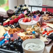 A festive Fourth of July Snack Board featuring berries, pretzels, dip, desserts, and small American flags, all beautifully arranged on a tray near a window.