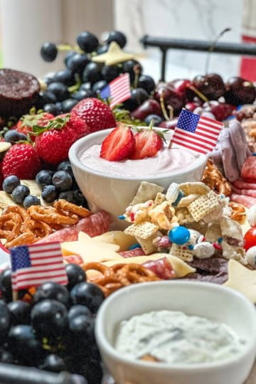 A festive Fourth of July Snack Board featuring berries, pretzels, dip, desserts, and small American flags, all beautifully arranged on a tray near a window.