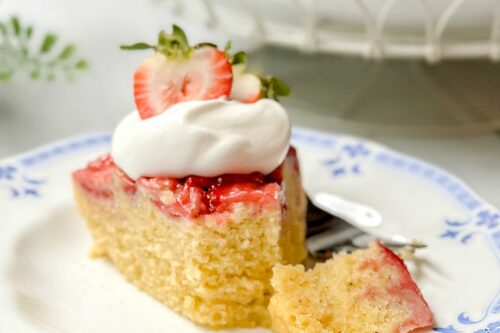 Side view of strawberry cake on a blue and white plate with a bite missing.
