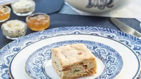 A small square biscuit sits on a decorative blue and white plate, surrounded by fine china, a teapot, and small jars of spread—perfect for a charming Father's Day tea party.