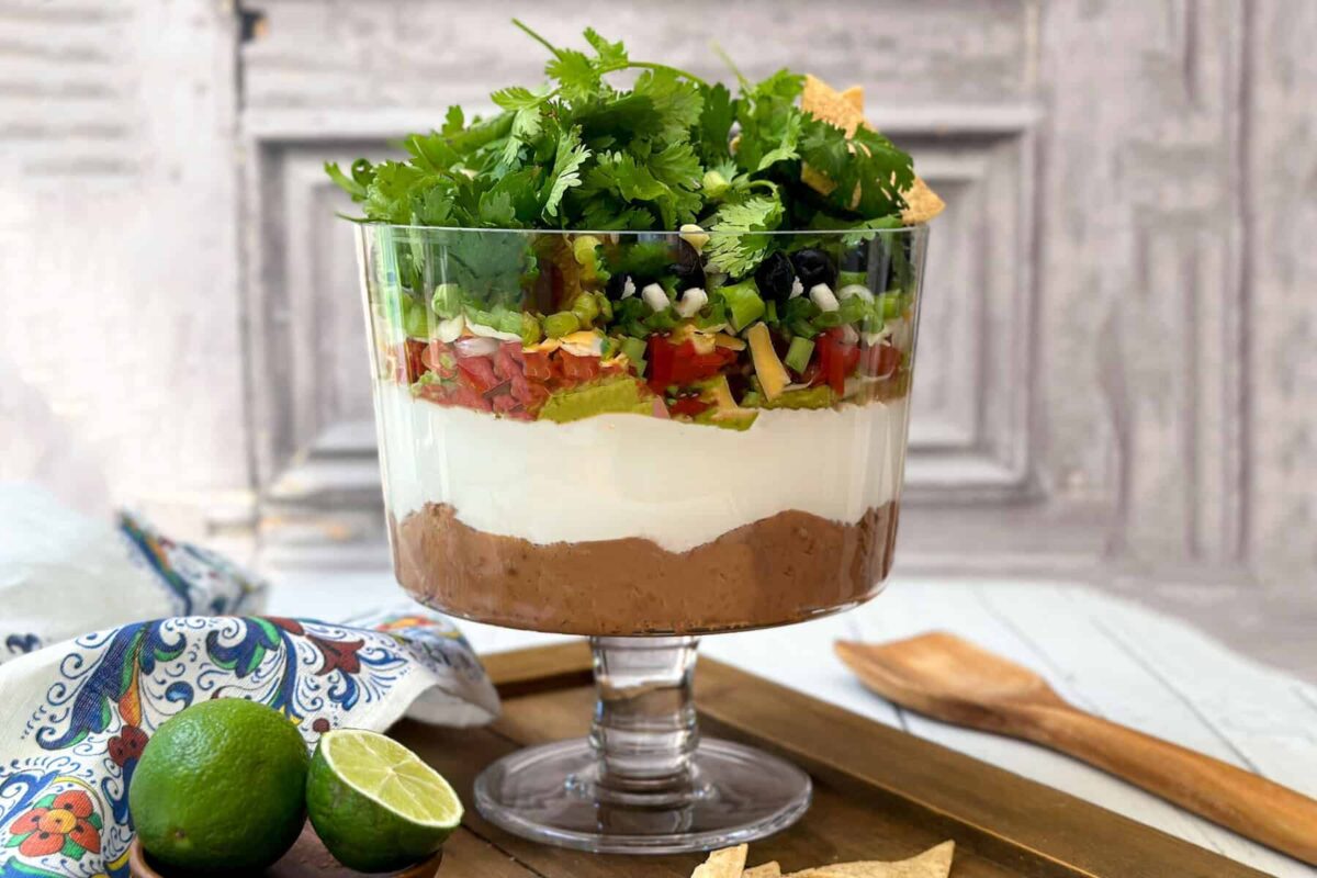 Horizontal view of easy 7 Layer Dip in a glass trifle dish with tortilla chips.