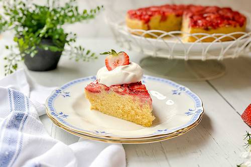 Horizontal side view of Strawberry Upside Down Cake with whipped cream and a sliced strawberry for serving.